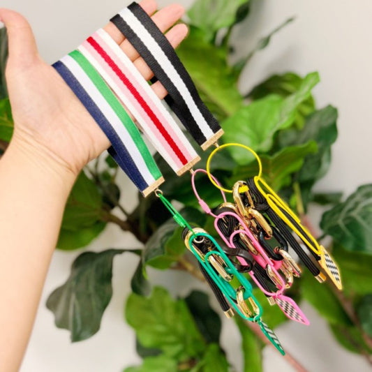 Hand holding a colorful keychain with multiple keychains attached, against a green leafy background.