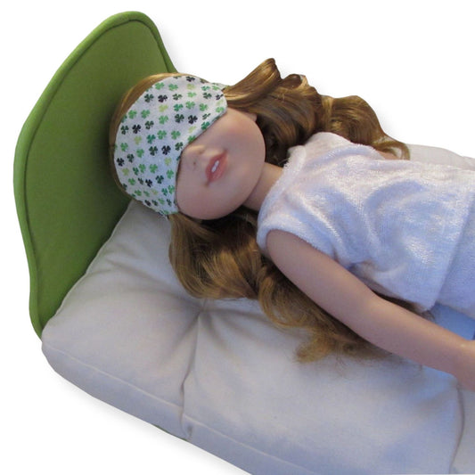 Doll wearing a green sleep mask with clover pattern on a white background