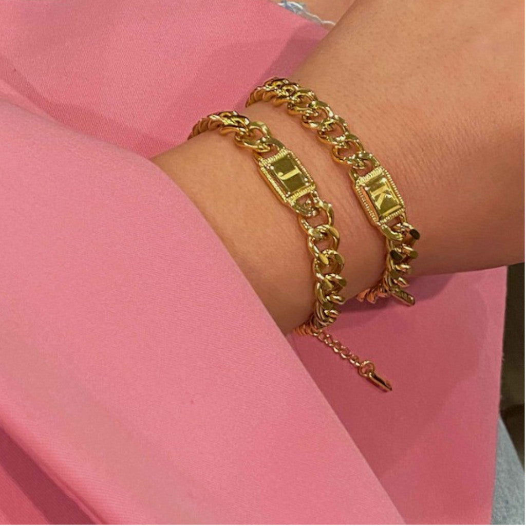 J and K Initial Gold Cuban Chain bracelets on wrist pink background