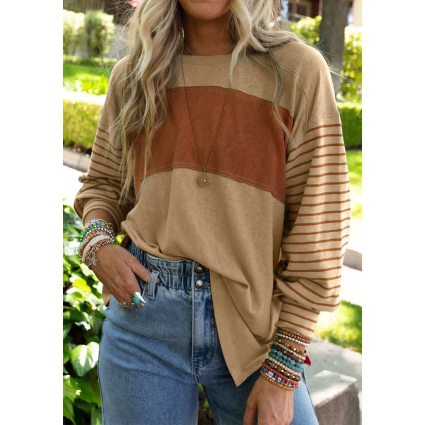 Person wearing a beige and brown color-blocked sweater with striped sleeves, standing outdoors.