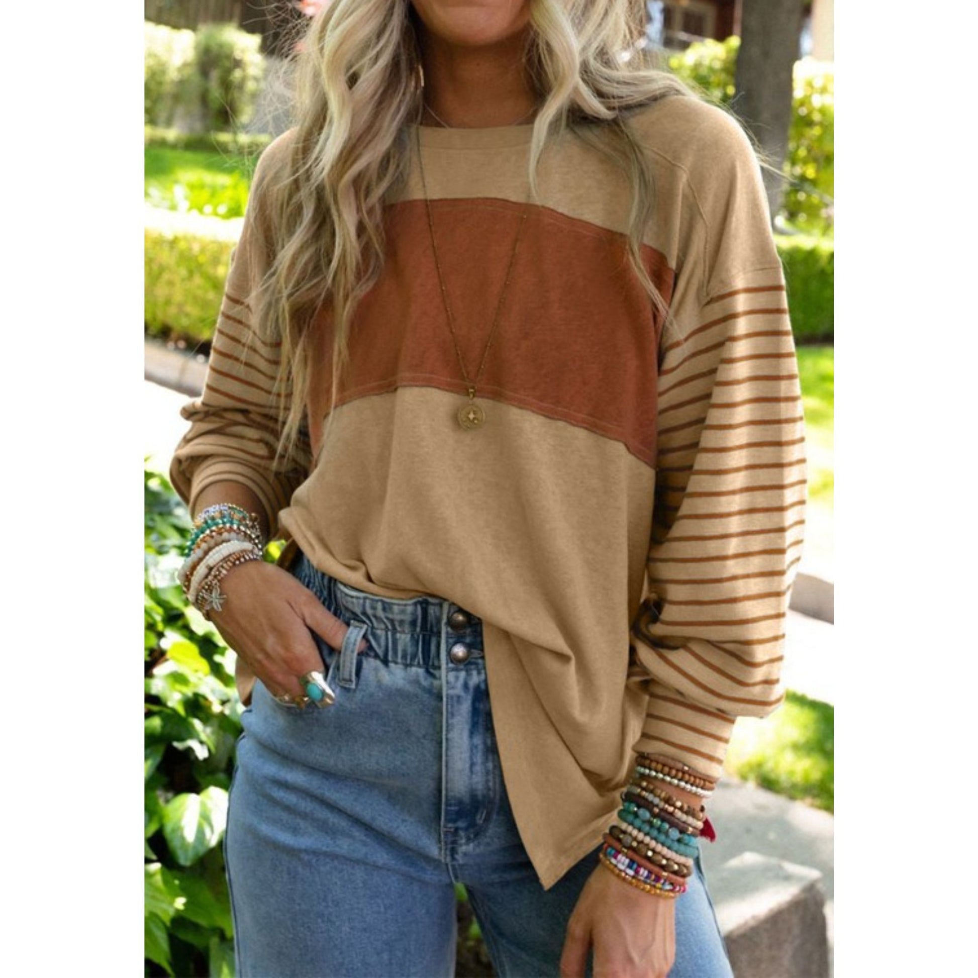 Person wearing a beige and brown color-blocked sweater with striped sleeves, standing outdoors.
