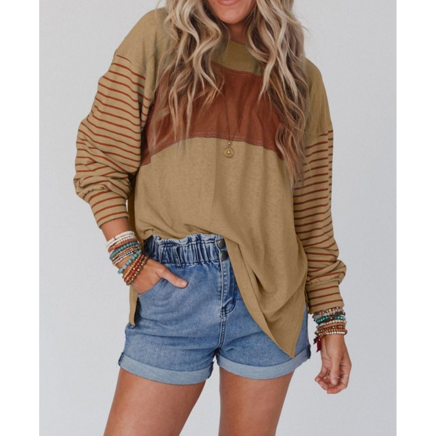 Person wearing a brown and beige color-blocked sweater with striped sleeves and denim shorts on a plain background.