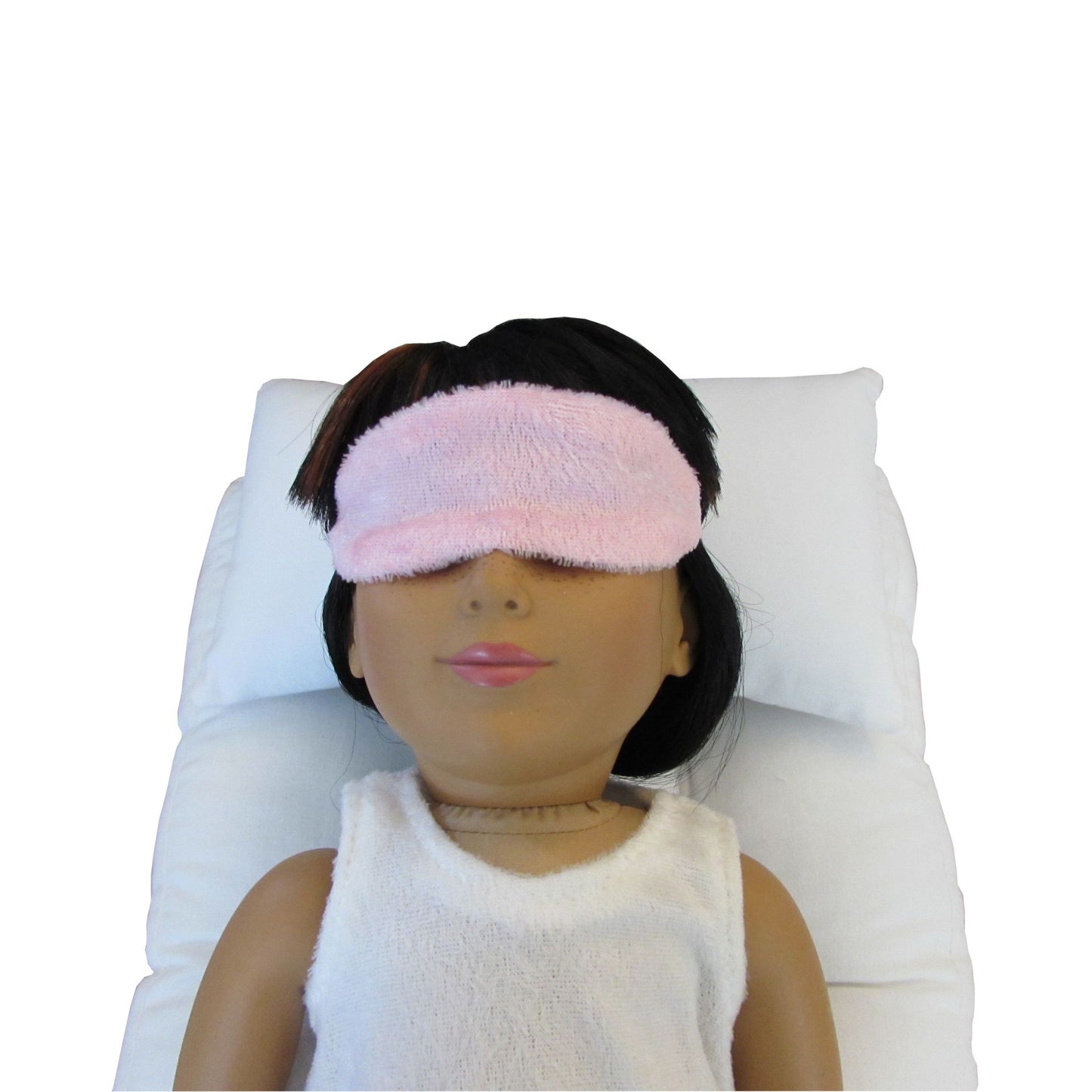 An 18-inch doll wearing a light pink panne velvet doll sleep mask while lying on a white doll pillow and a white doll mattress.
