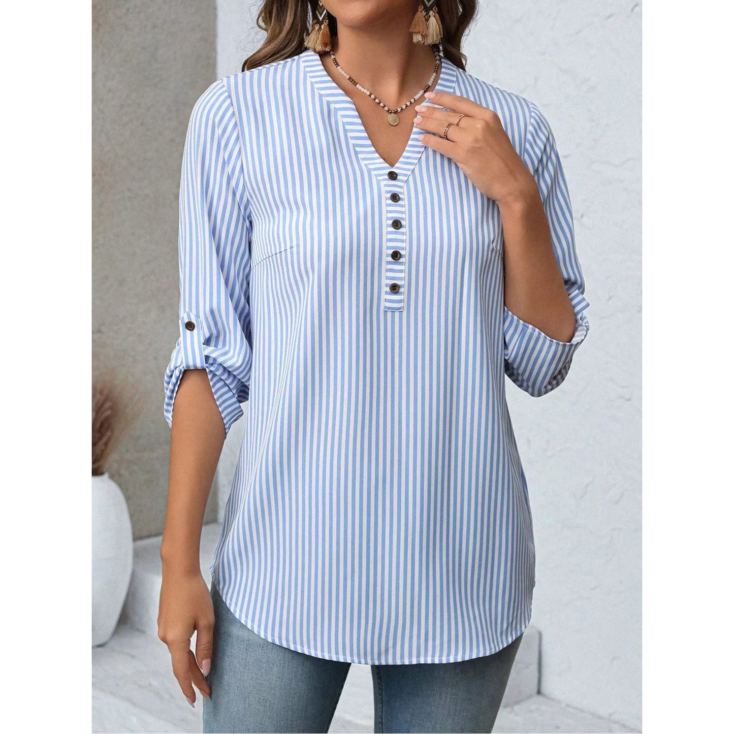Woman wearing a blue and white striped shirt with rolled-up sleeves against a neutral background