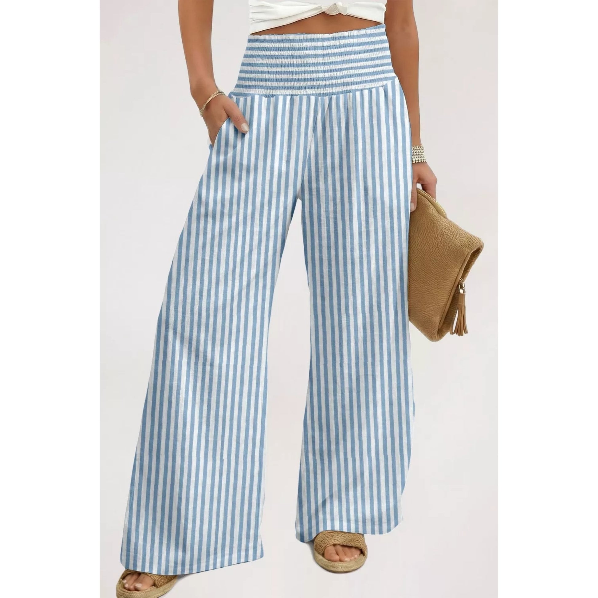 A person wearing light blue and white vertically striped wide-leg pants, holding a tan woven clutch against a plain light background.