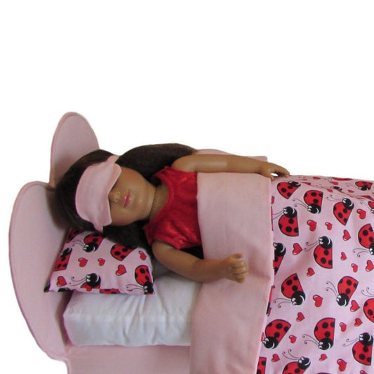 Doll in bed with pink bedding and ladybug pattern, wearing a red shirt and pink sleep mask.