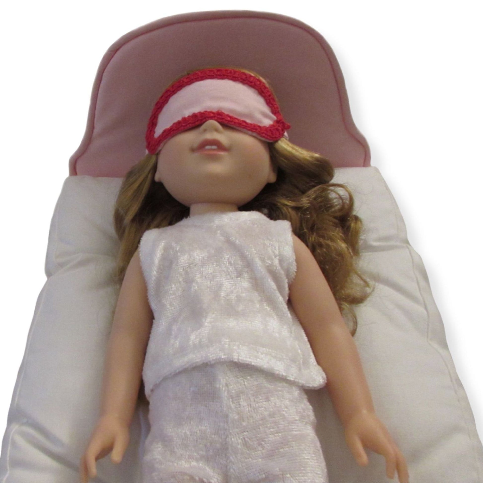 Doll wearing a white outfit and red trimmed pink sleep mask on a white background