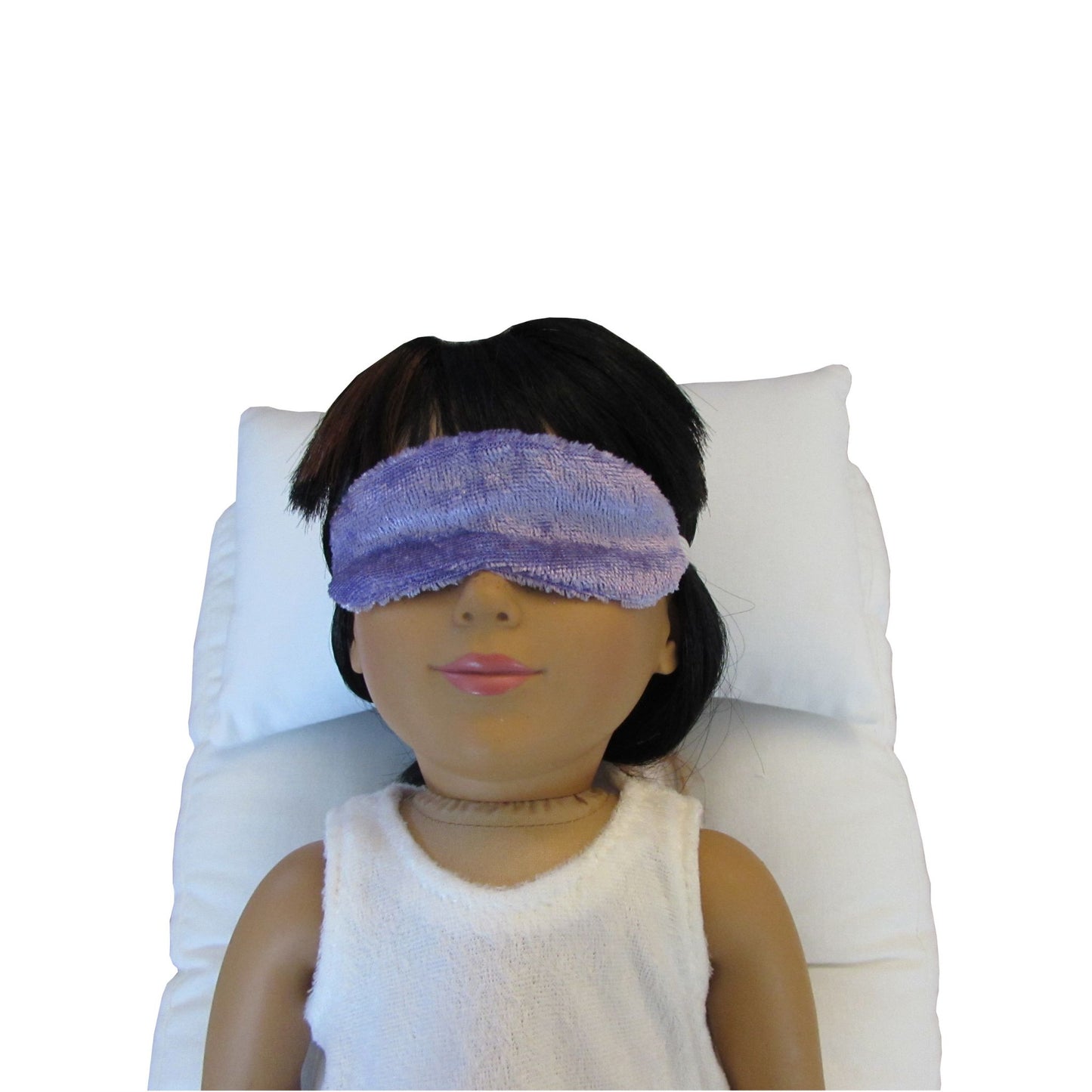 An 18-inch doll is wearing a lilac panne velvet sleep mask while lying on a white doll pillow and a white doll mattress.