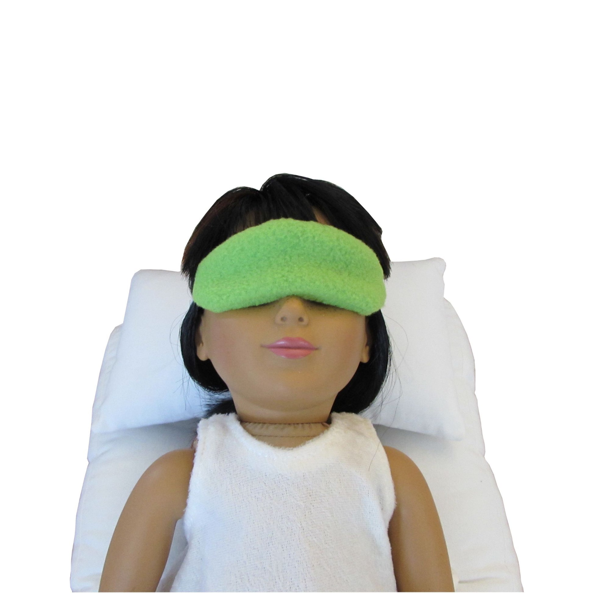 An 18-inch doll is wearing a lime colored anti-pill fleece sleep mask while lying on a white doll pillow and doll mattress.