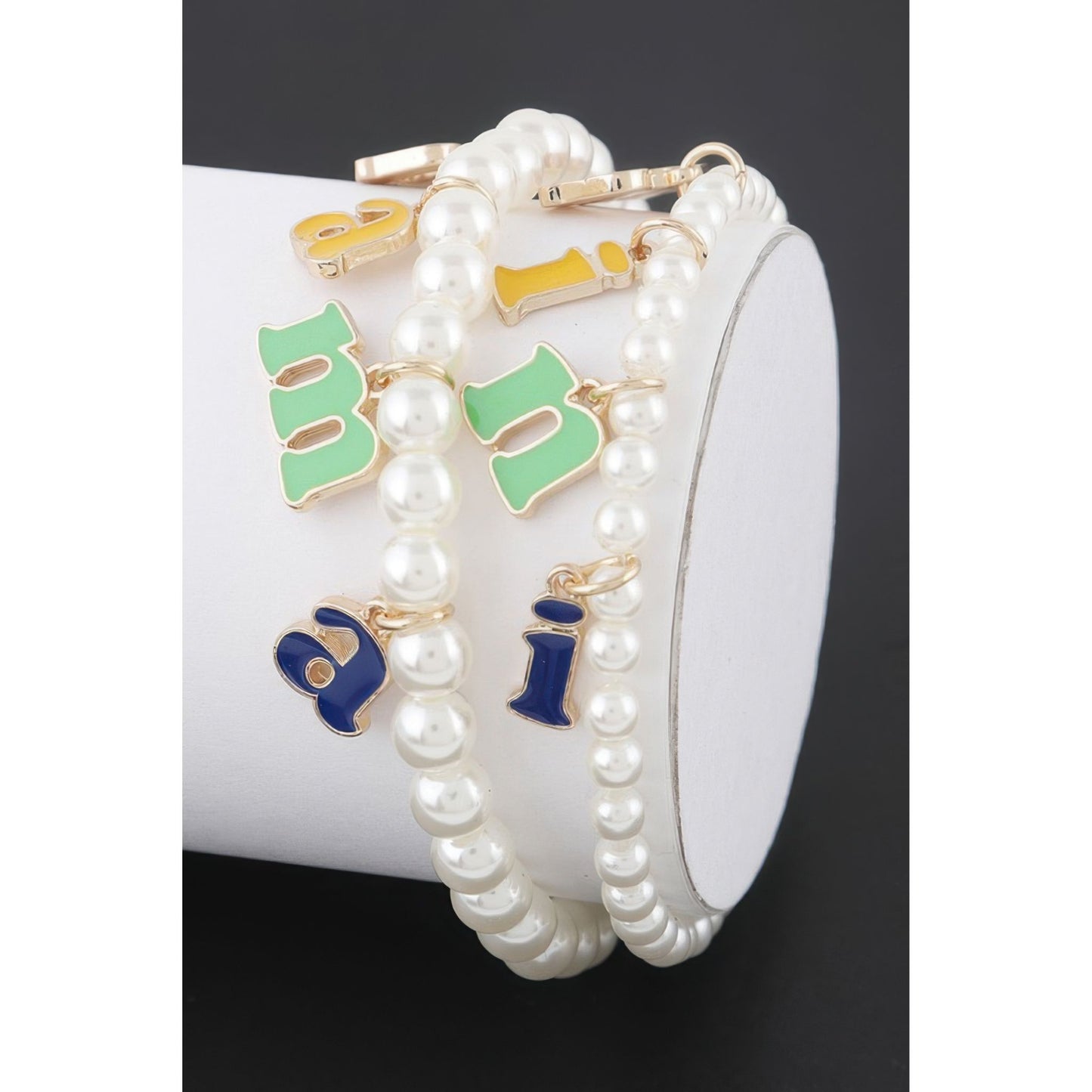 Pearl bracelet with colorful letter charms on a white cylindrical container.