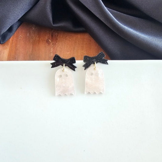 Ghost-shaped earrings with black bow details on a white surface.