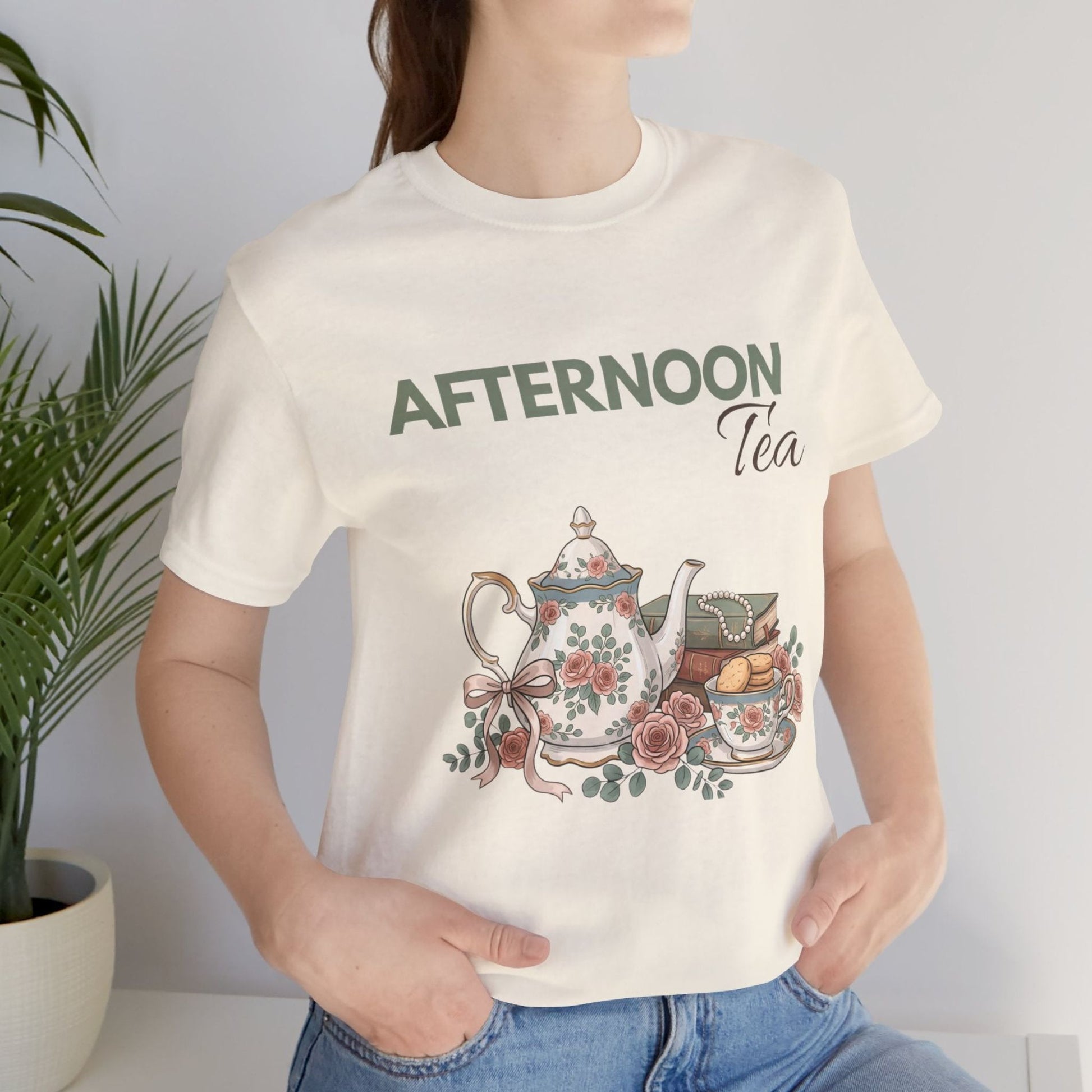 A woman standing by a plant with a natural colored t-shirt with 'AFTERNOON Tea' on the front.