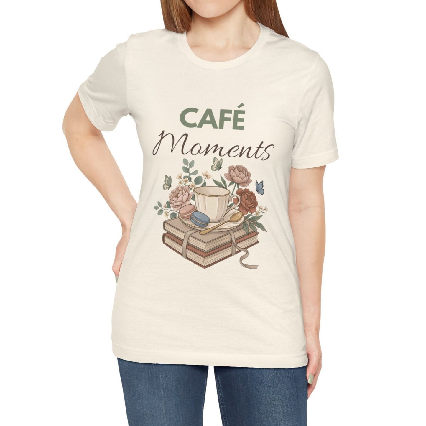 Person wearing a natural colored t-shirt with 'Café Moments' design featuring a coffee cup and books.