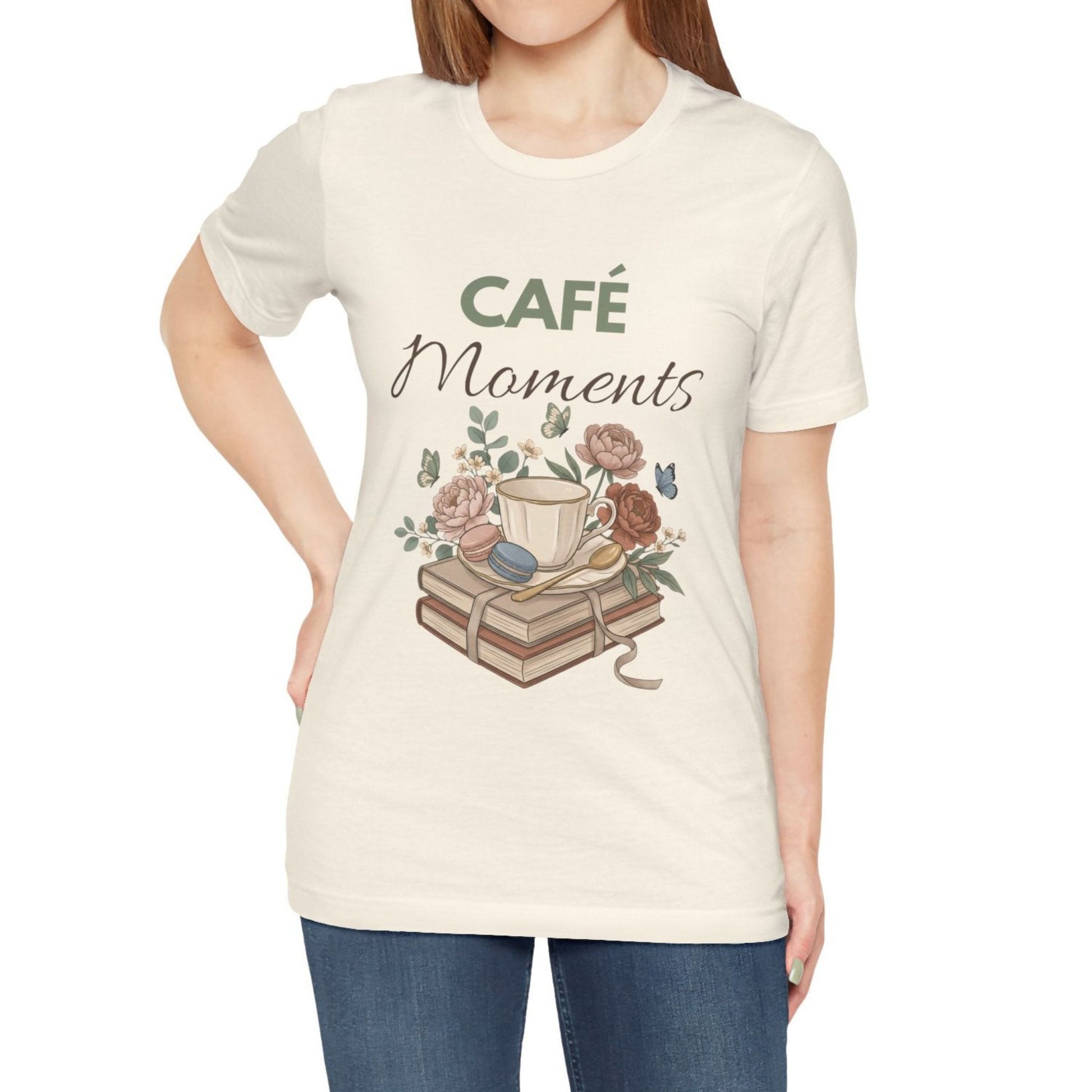 Person wearing a natural colored t-shirt with 'Café Moments' design featuring a coffee cup and books.