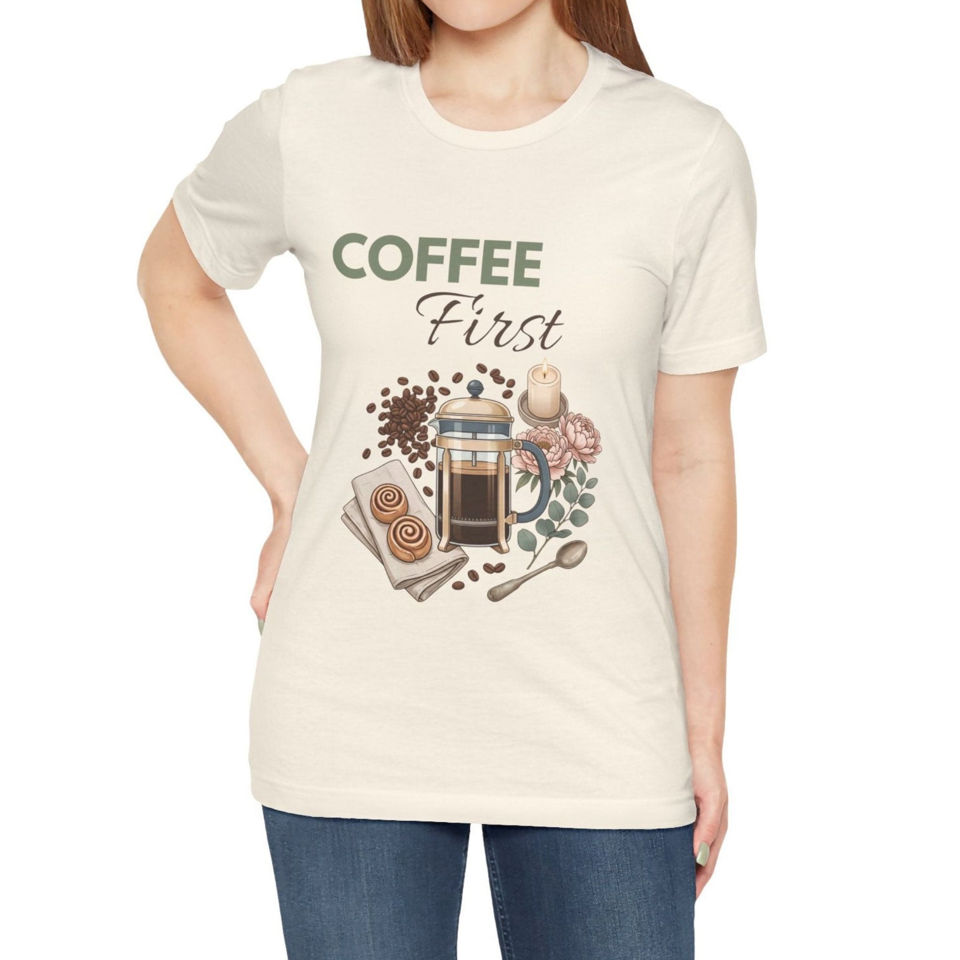 Person wearing a natural colored t-shirt with a coffee-themed graphic and 'Coffee First' text.