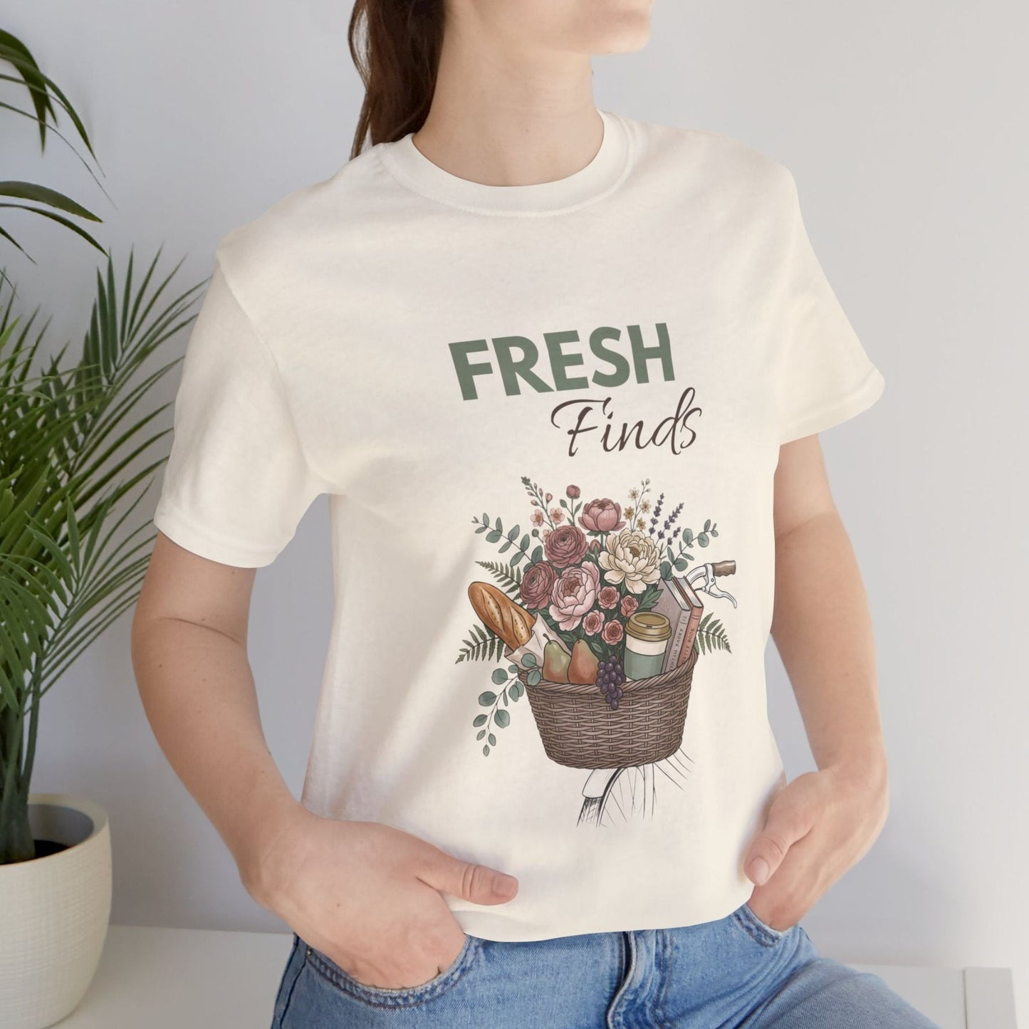 A woman standing by a plant with a t-shirt with 'FRESH Finds' on the front.
