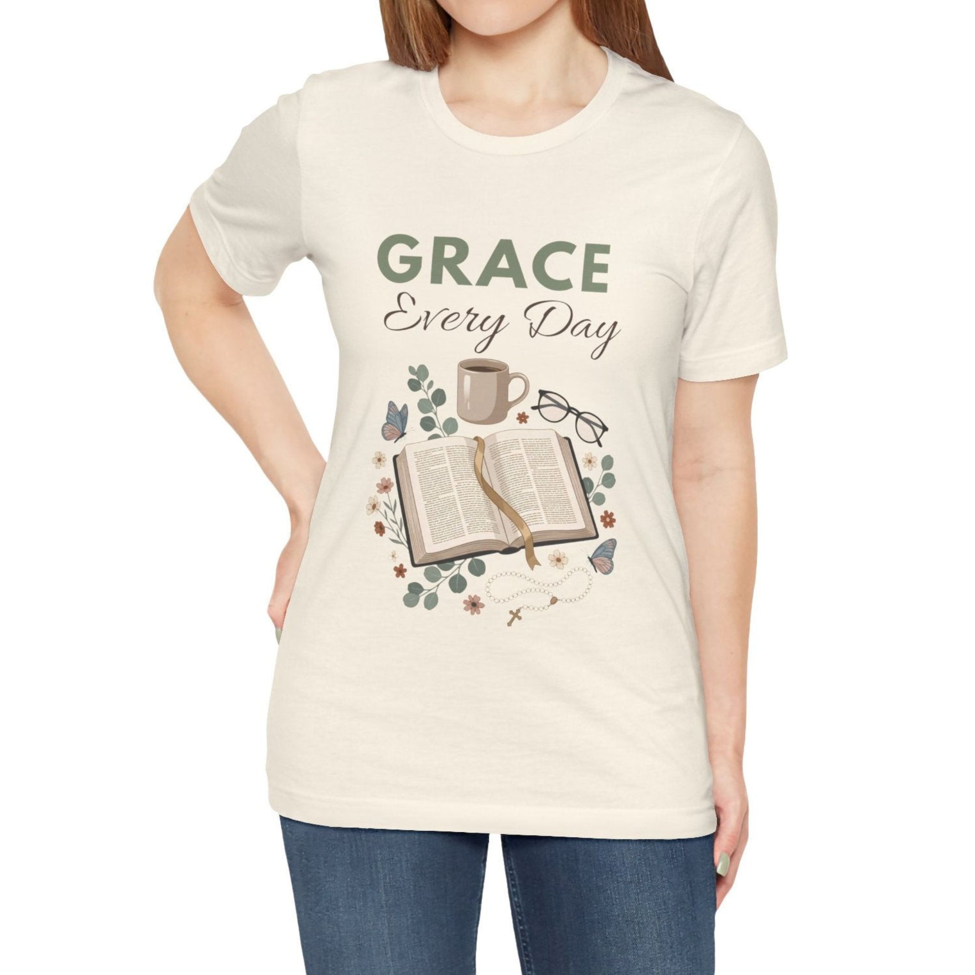 Person wearing a natural colored t-shirt with 'Grace Every Day' design featuring a book, coffee cup, and glasses.