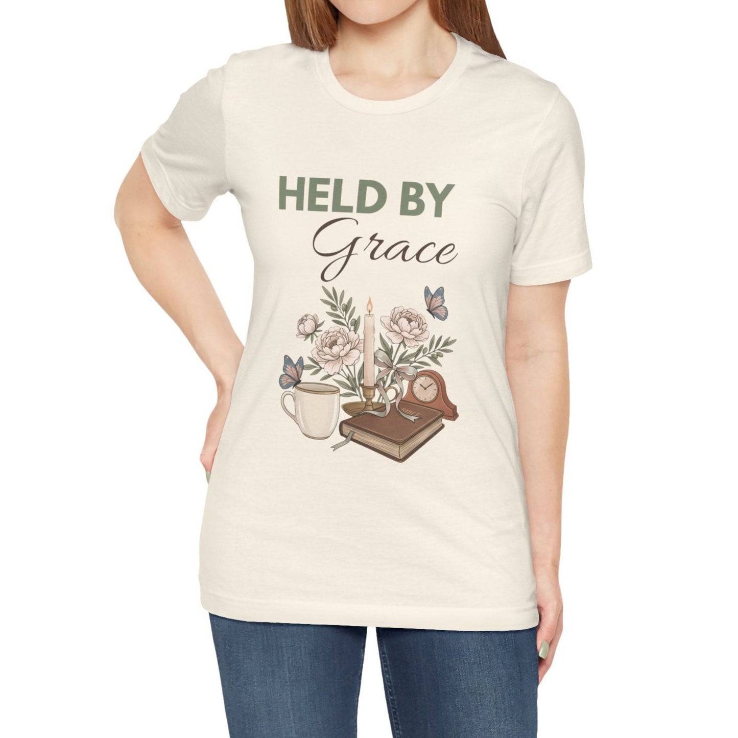 A woman wearing a natural colored t-shirt with "Held by Grace".