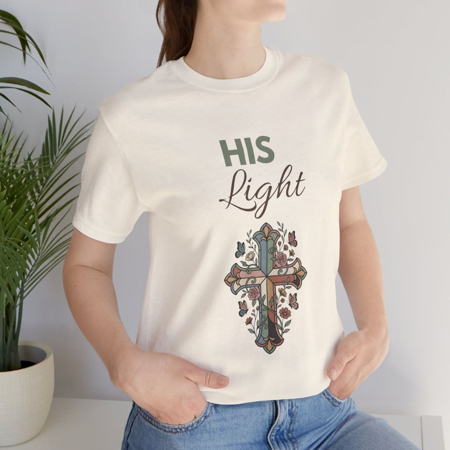 Person wearing a natural colored t-shirt with a cross design and 'HIS Light' text, standing against a plain background.