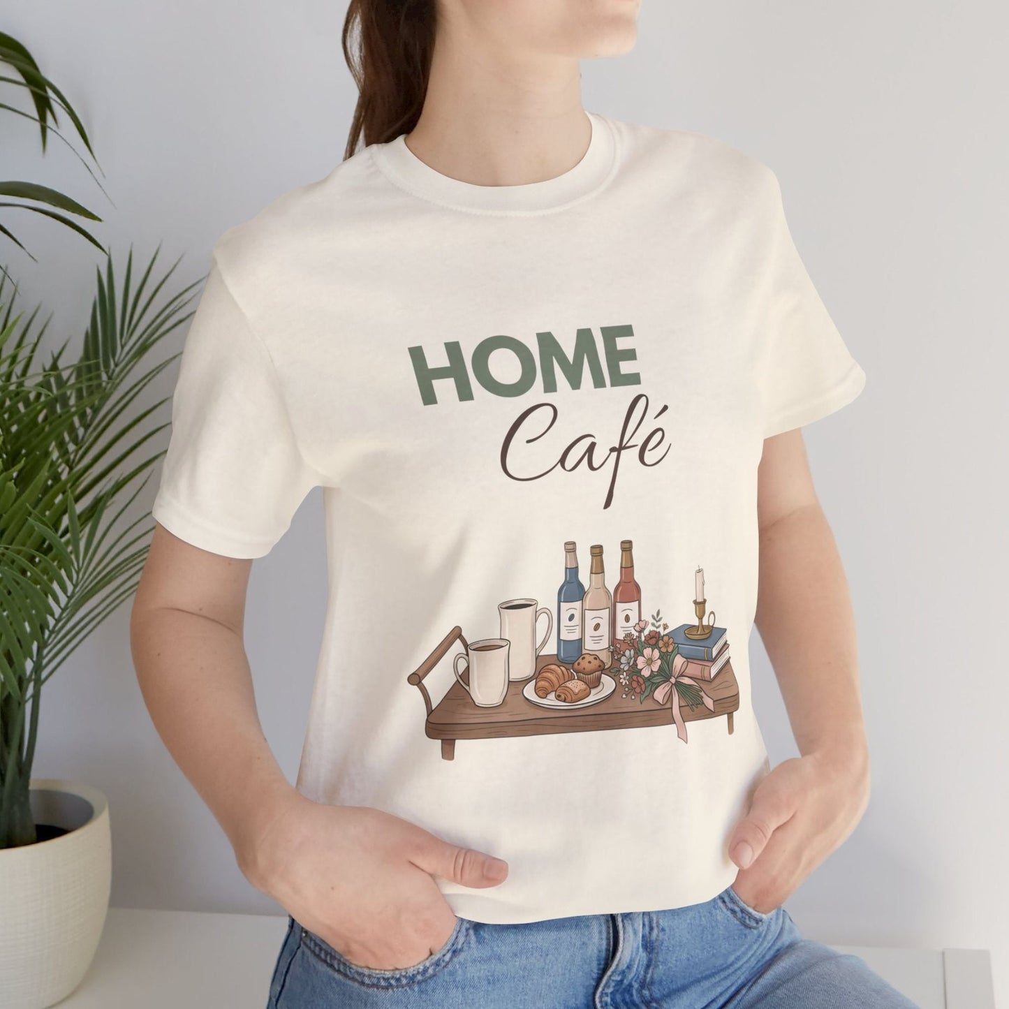 Person wearing a natural colored t-shirt with 'HOME Café' design featuring a table with bottles and food.