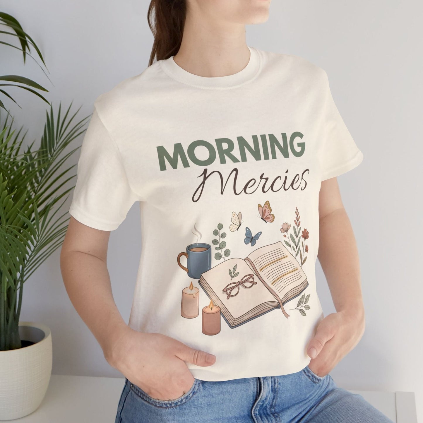 Person wearing a natural colored t-shirt with 'Morning Mercies' design, holding a plant.