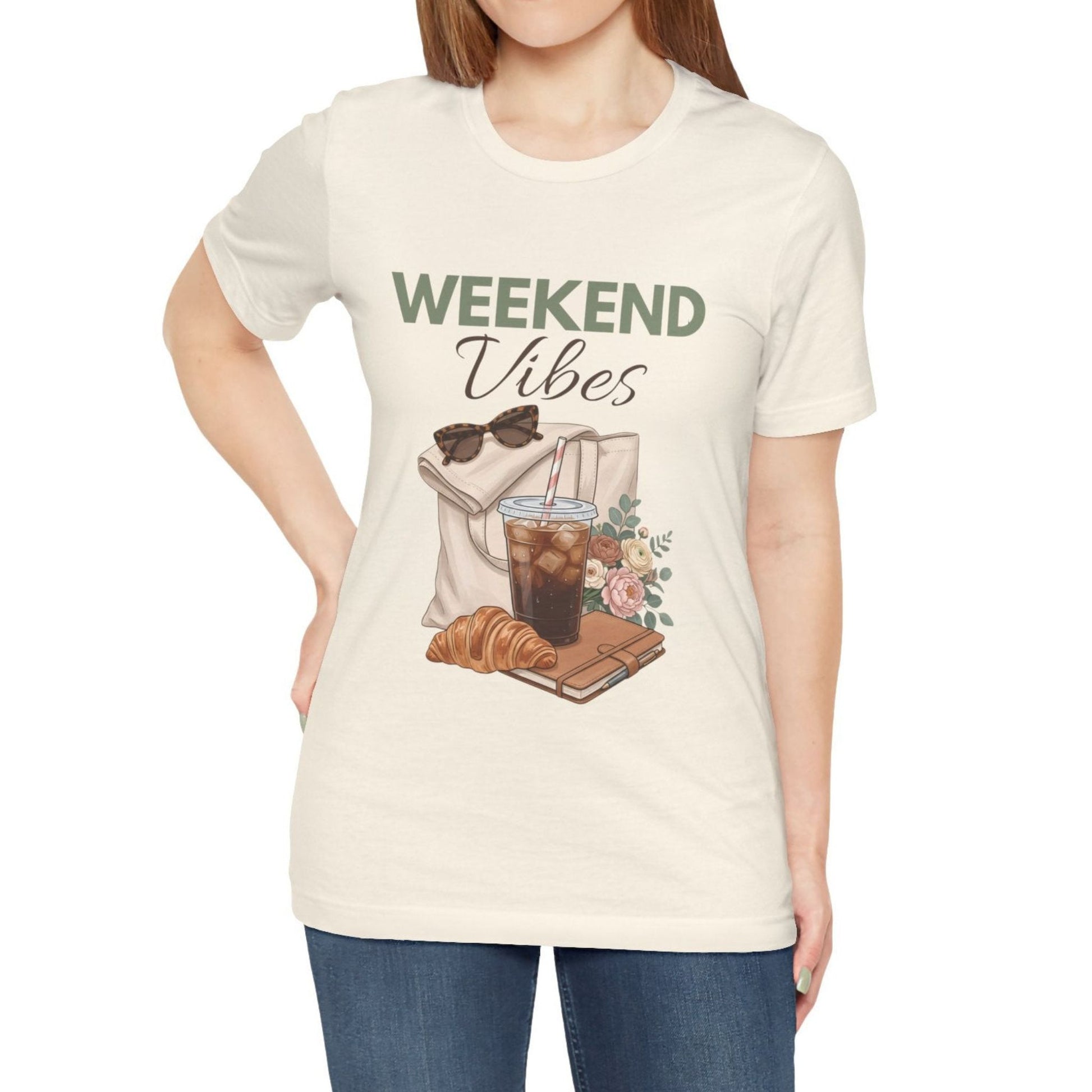 Person wearing a natural colored t-shirt with 'Weekend Vibes' design featuring a coffee cup, croissant, and sunglasses.