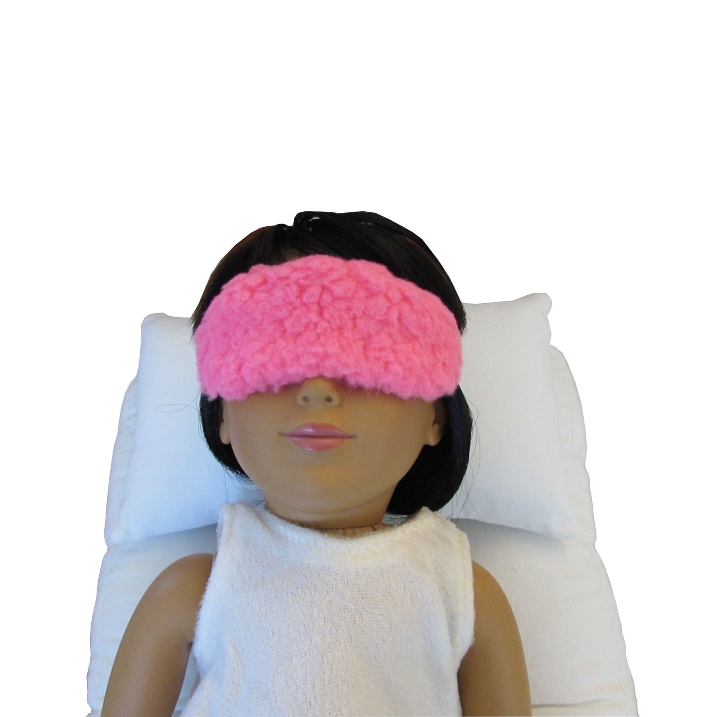 A 18-inch doll is wearing a neon pink faux sherpa fur sleep mask while lying on a white doll pillow and a doll mattress.