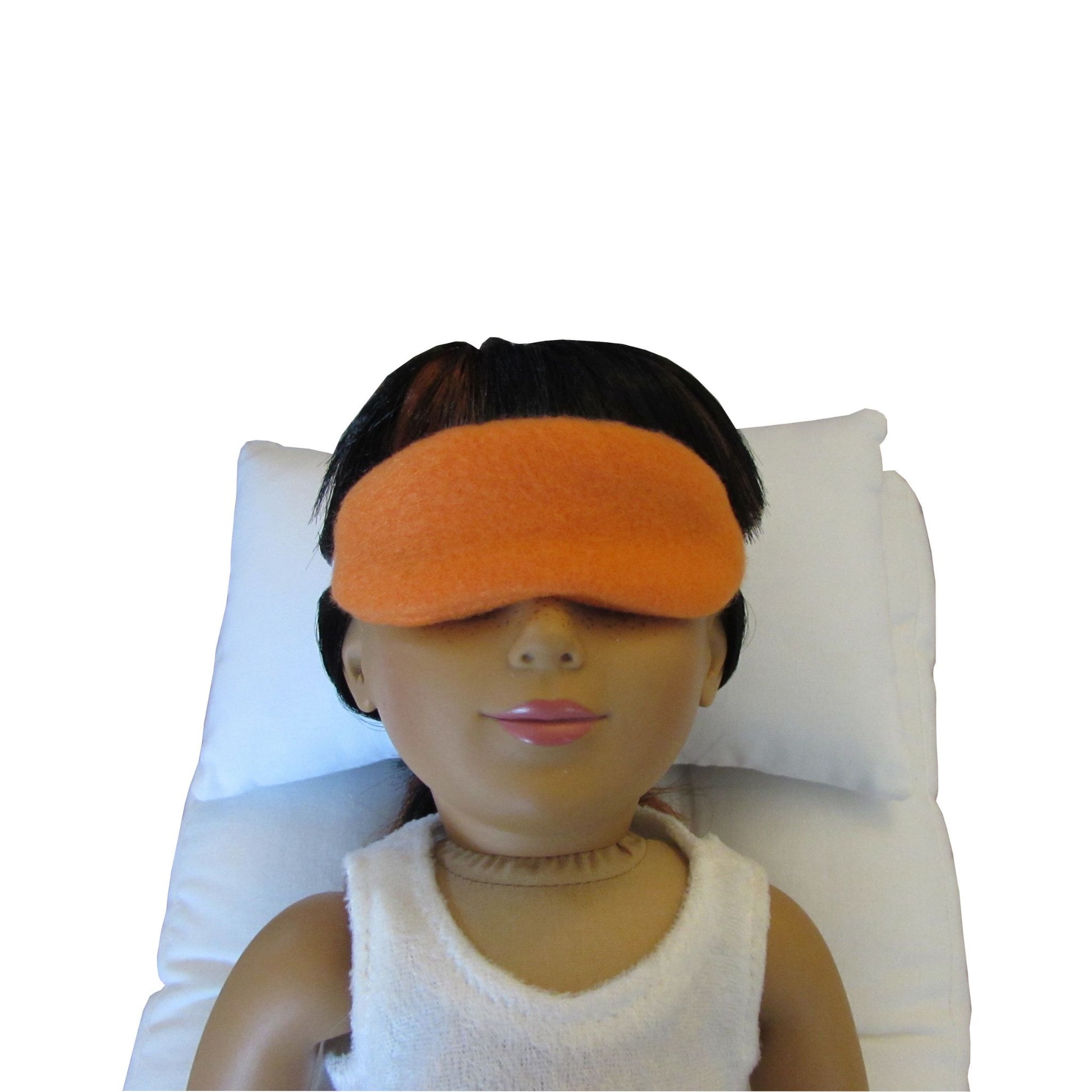 An 18-inch doll wearing an orange anti-pill fleece sleep mask while lying on a white doll pillow and a white doll mattress.