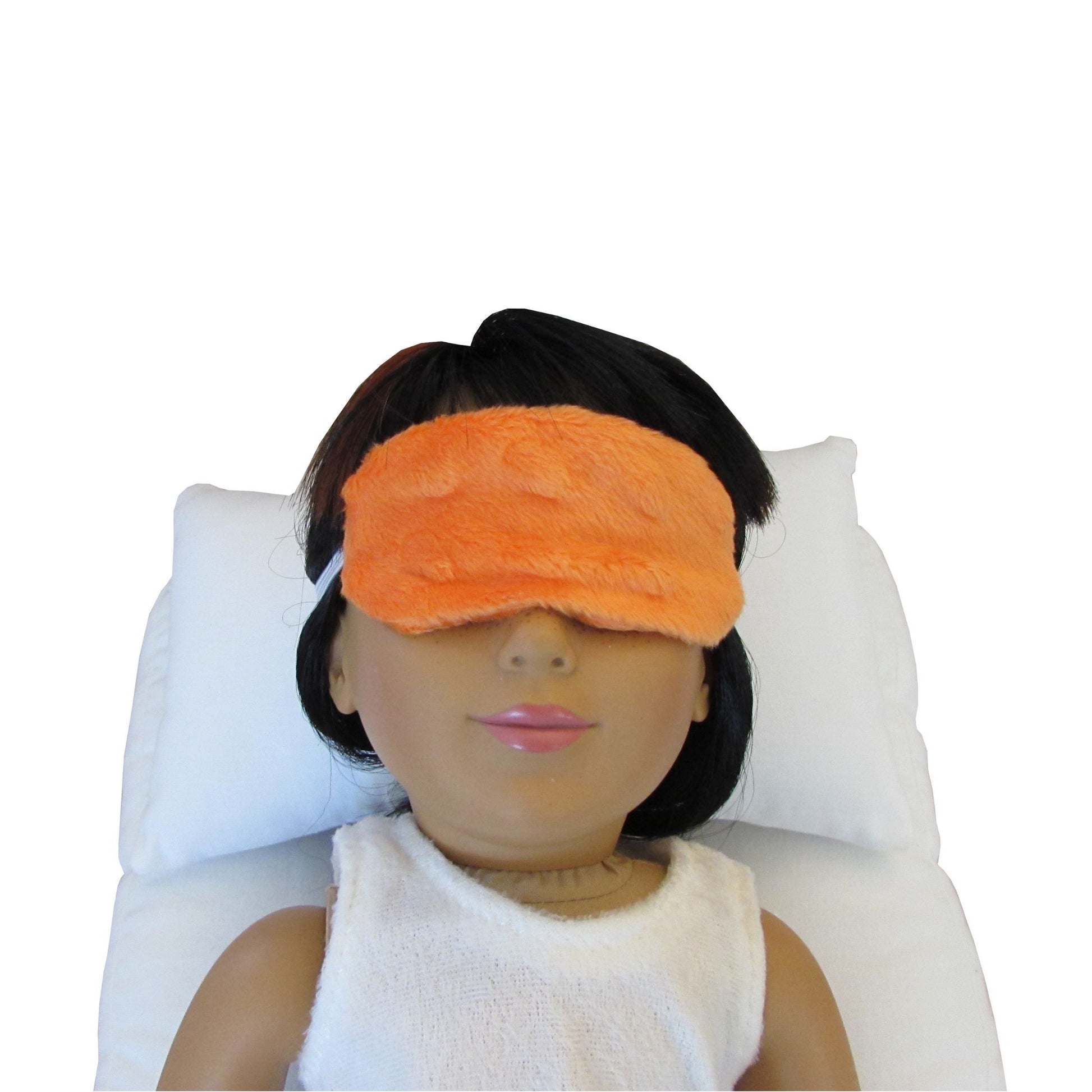 An 18-inch doll is wearing an orange sleep mask while lying on a white doll pillow and a white doll mattress.