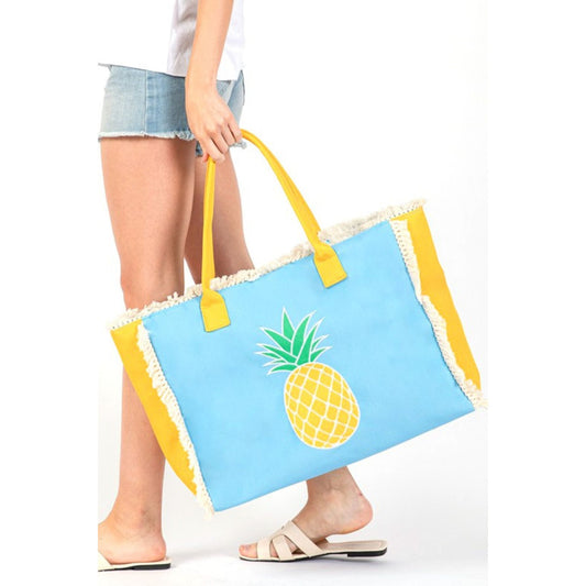 Person holding a blue beach bag with a pineapple design and yellow handles.
