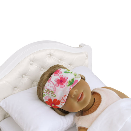 Doll wearing a floral sleep mask on a white bed