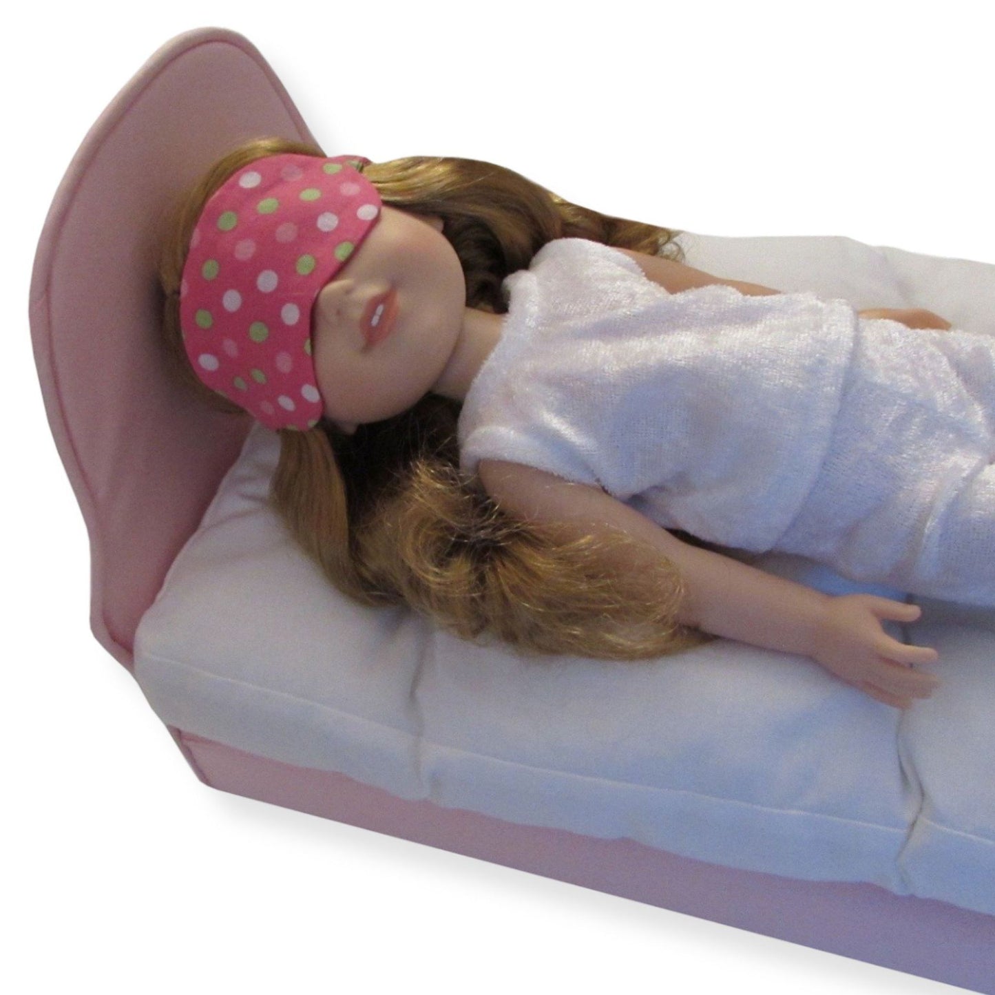 A 14.5-inch doll wearing a pink polka dot eye mask, lying on a white doll bed.