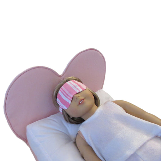 Doll lying on a pink heart-shaped pillow with a striped eye mask on a white background