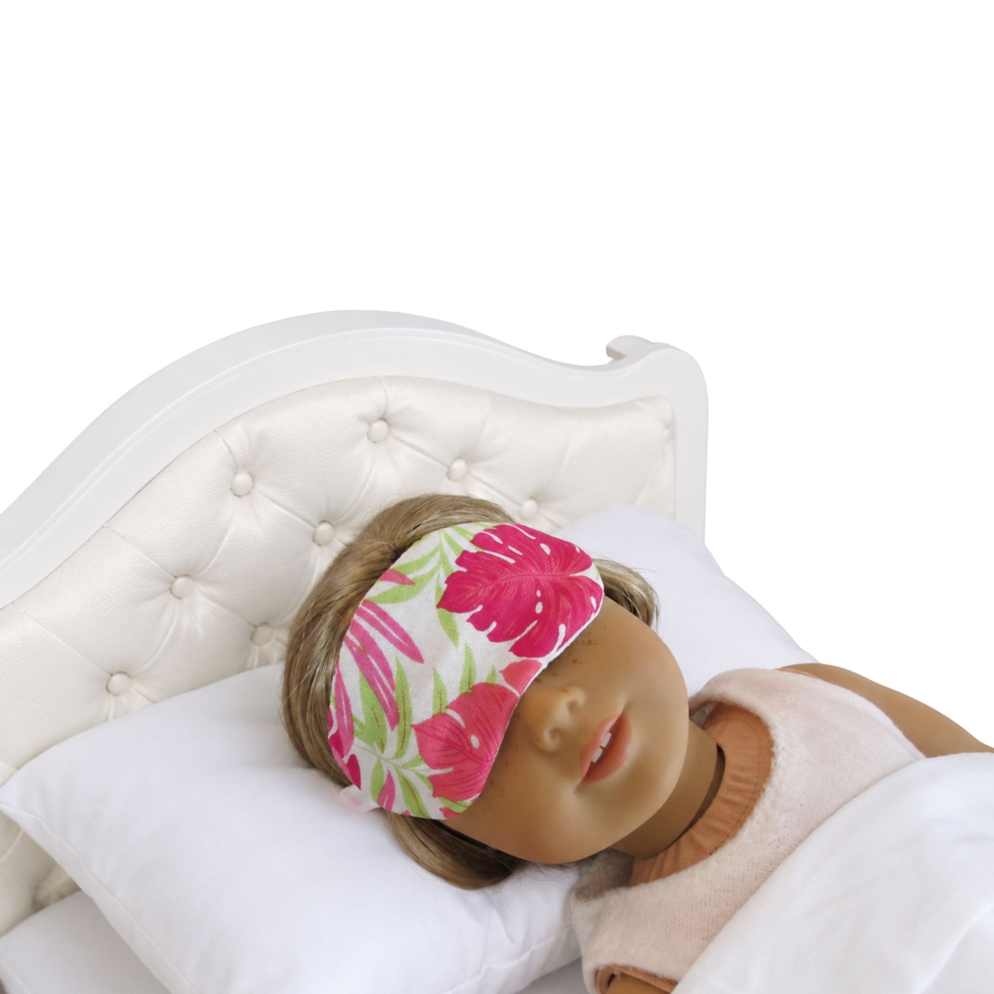 Doll wearing a floral sleep mask on a white bed