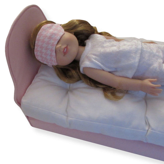 A 14.5-inch doll wearing a gingham print sleep mask while lying on a pink bed.