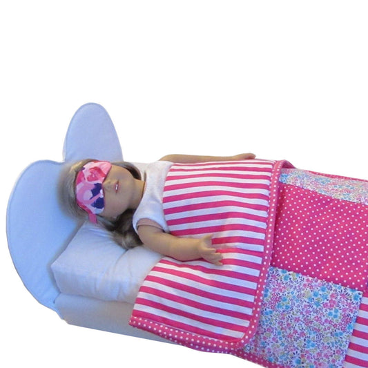 Doll lying in bed with a pink and white striped blanket and floral quilt.