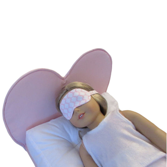 An 18-inch doll wearing a pink print sleep mask while lying on a heart-shaped doll bed.