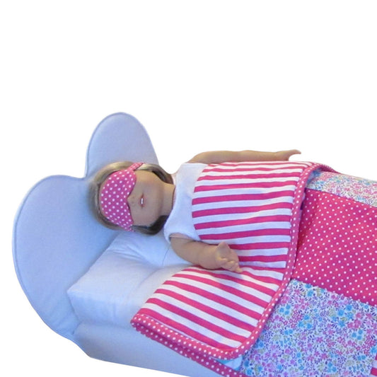 An 18-inch doll wearing a pink sleep mask with white small dots while lying on a heart doll bed.