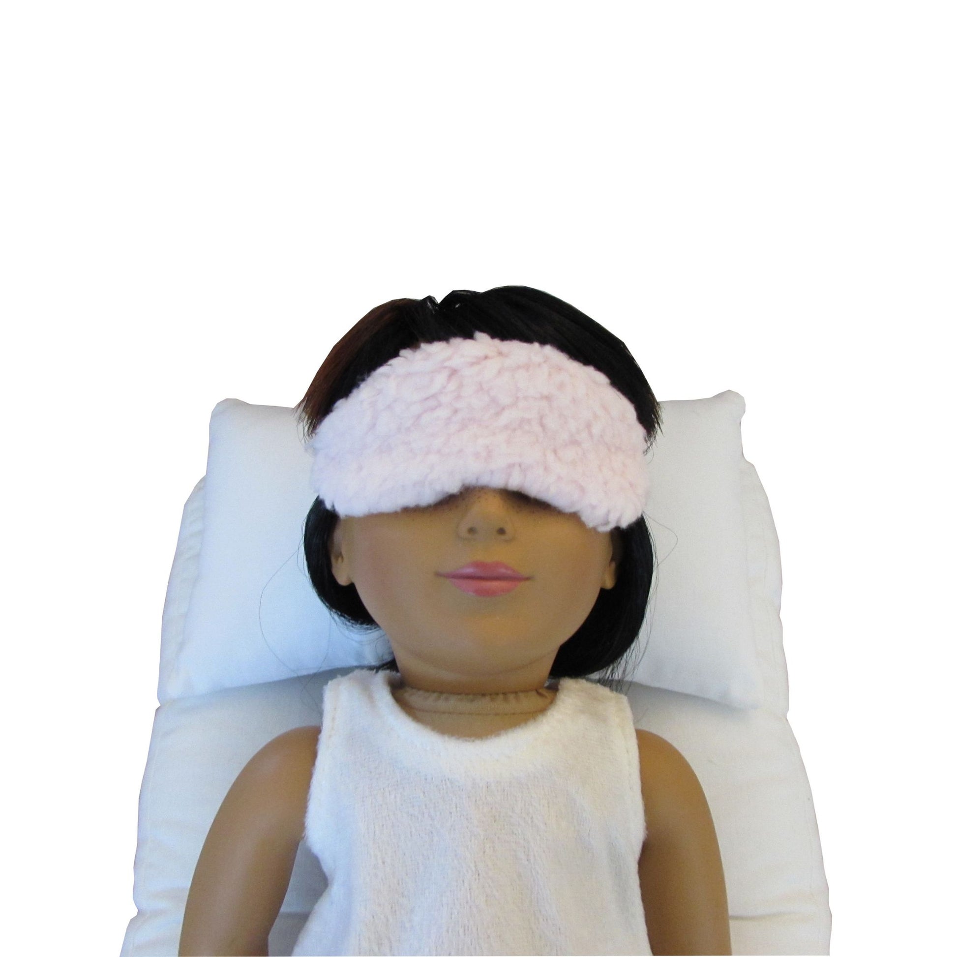 A doll wearing a fluffy pink faux sherpa fur eye mask on a white background.