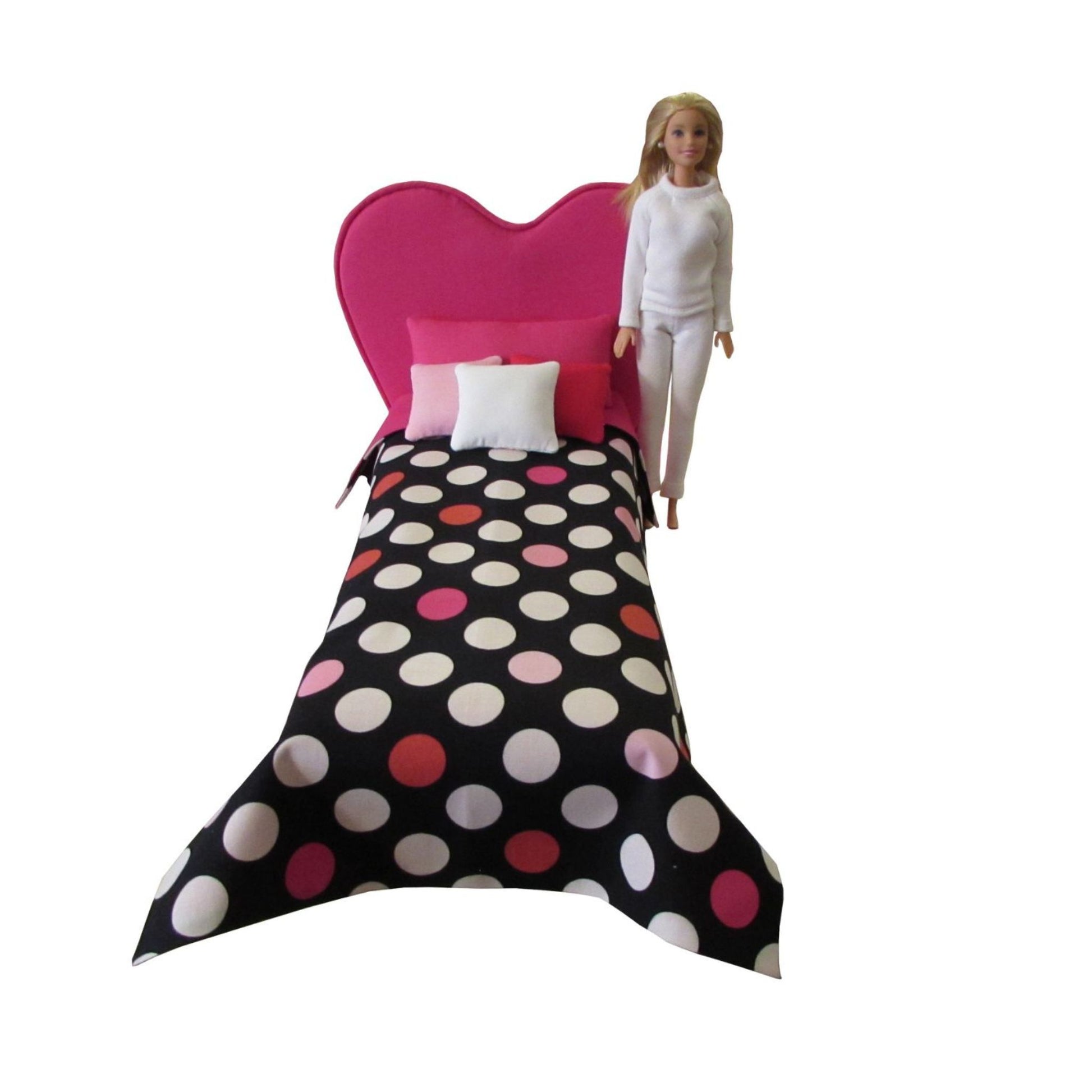 Barbie doll standing next to a bed with polka dot bedding and pink headboard on a white background
