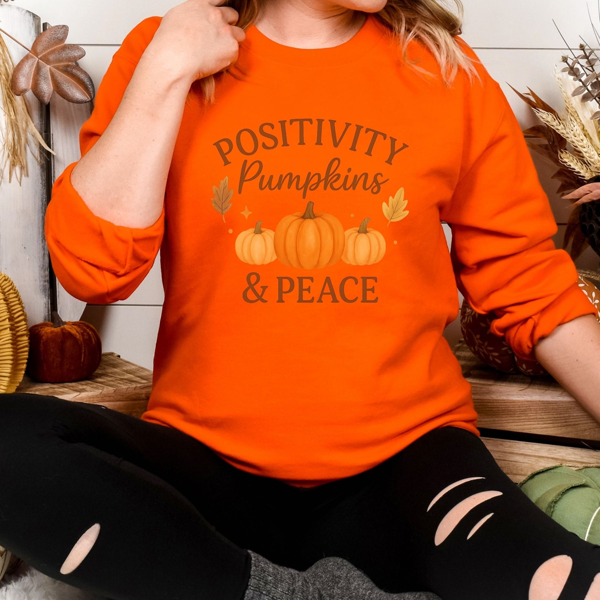 Person wearing an orange sweatshirt with 'Positivity Pumpkins & Peace' text and pumpkin graphics.