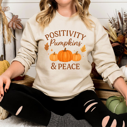 Person wearing a sand sweatshirt with 'Positivity Pumpkins & Peace' text and pumpkin graphics.