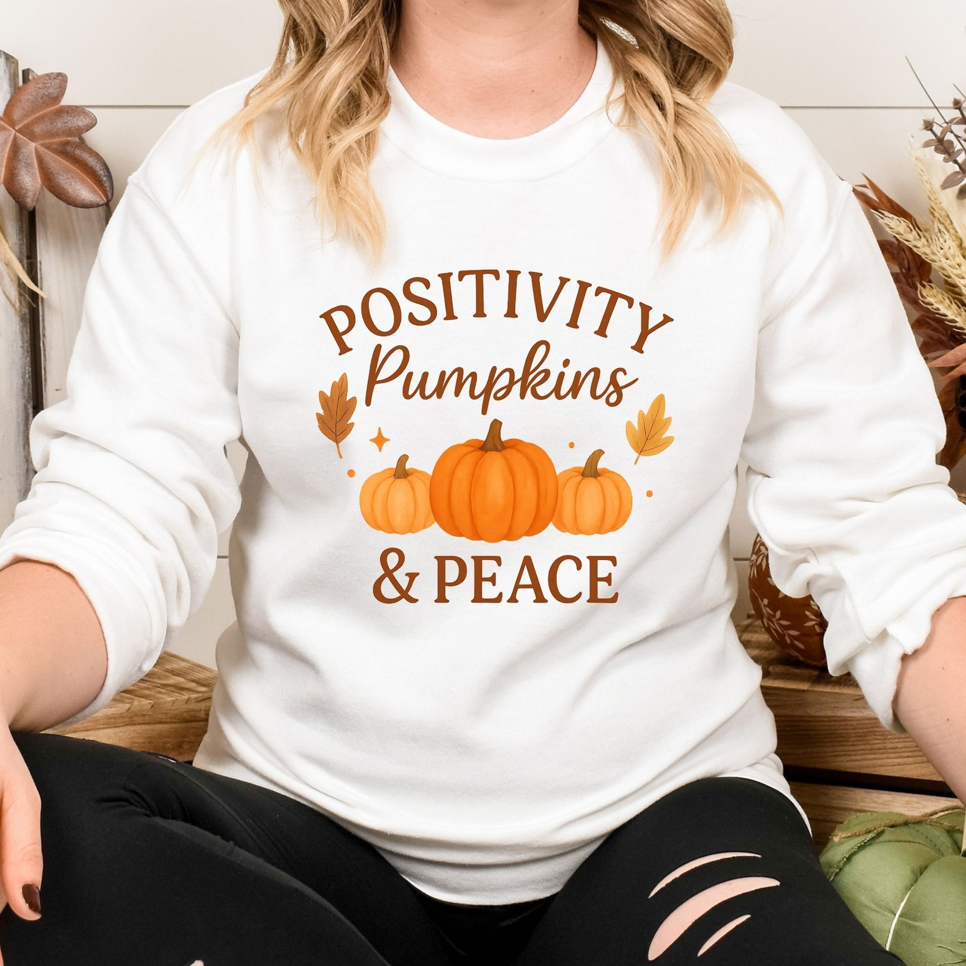 Person wearing a white sweatshirt with 'Positivity Pumpkins & Peace' text and pumpkin graphics.