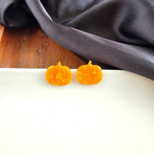 Two small pumpkin-shaped earrings on a white surface with a dark fabric background.