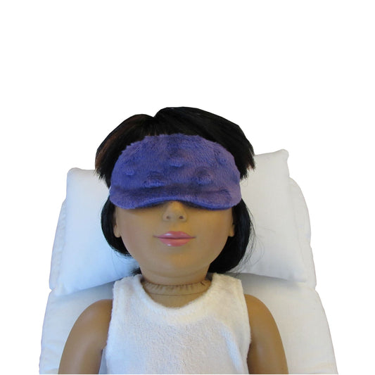 An 18-inch doll wearing a purple minky sleep mask while lying on a white doll pillow and a white doll mattress.