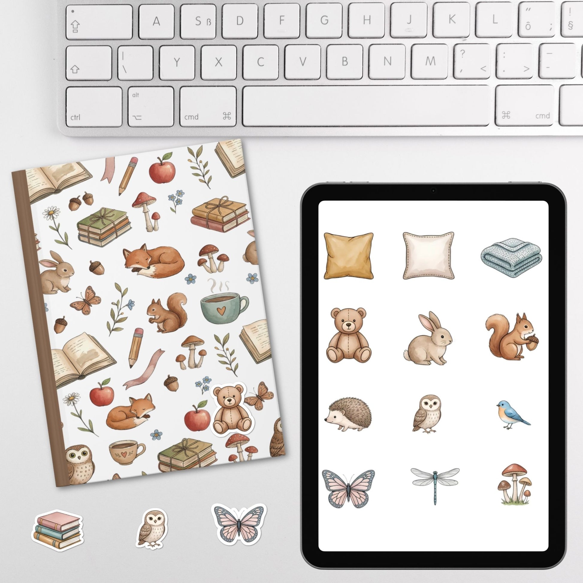 A flat-lay product presentation showing a notebook with a woodland animal pattern, a tablet displaying matching digital illustrations, and several individual sticker designs on a light gray surface below a white keyboard.