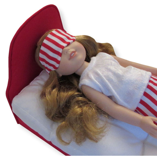 A 14.5-inch doll wearing a red striped sleep mask while lying on a red doll bed.