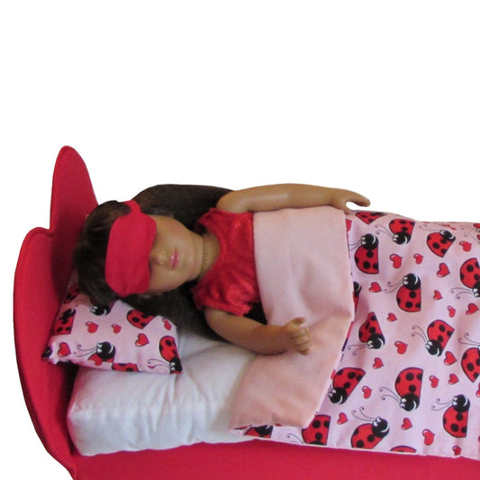 An 18-inch doll wearing a red sleep mask while lying on a red bed.
