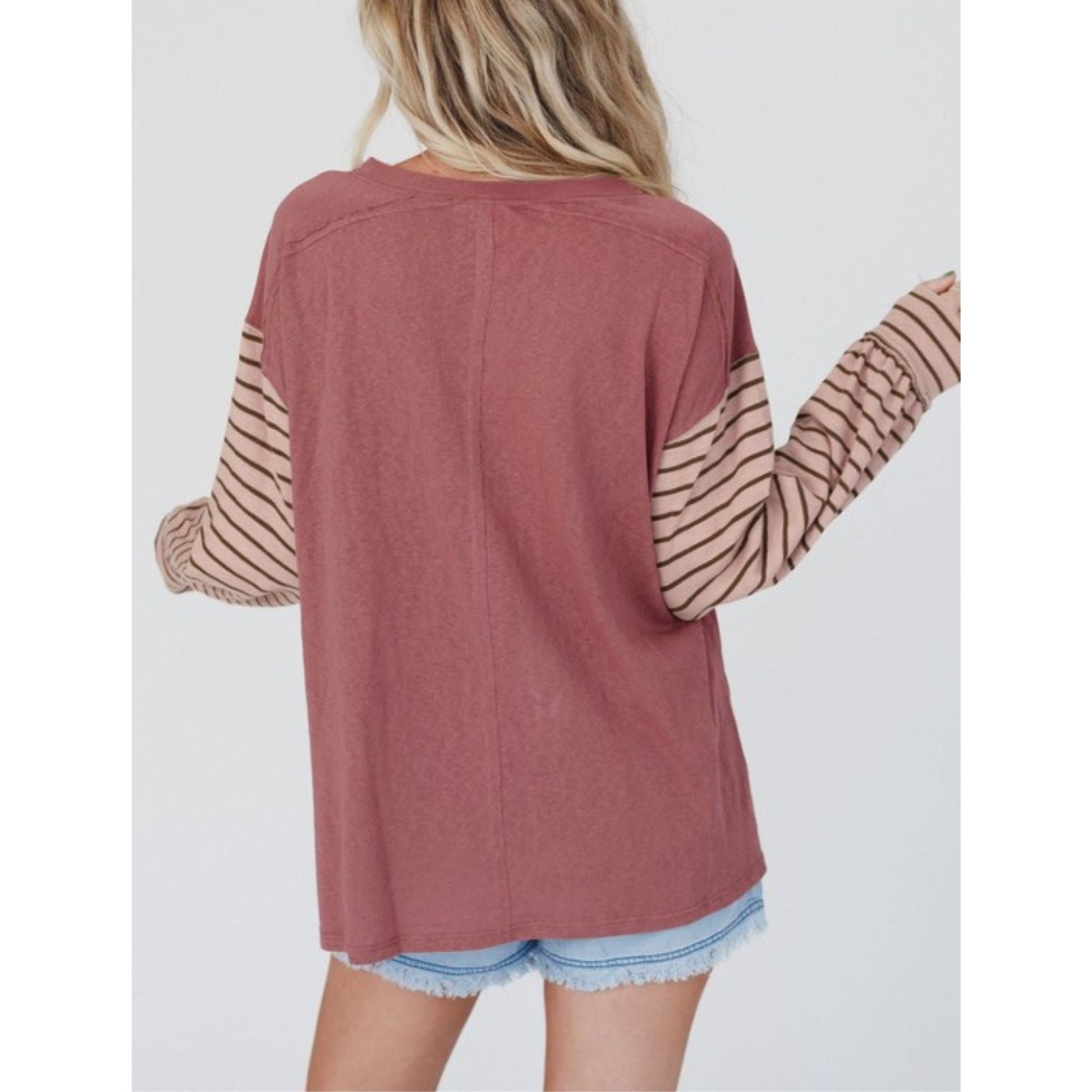 Person wearing a mauve long-sleeve top with sheer sleeves on a white background