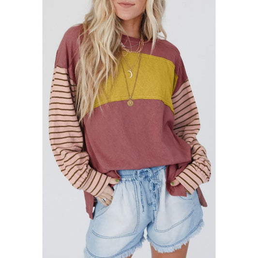 Woman wearing a color-blocked long-sleeve top with striped sleeves and denim shorts on a white background